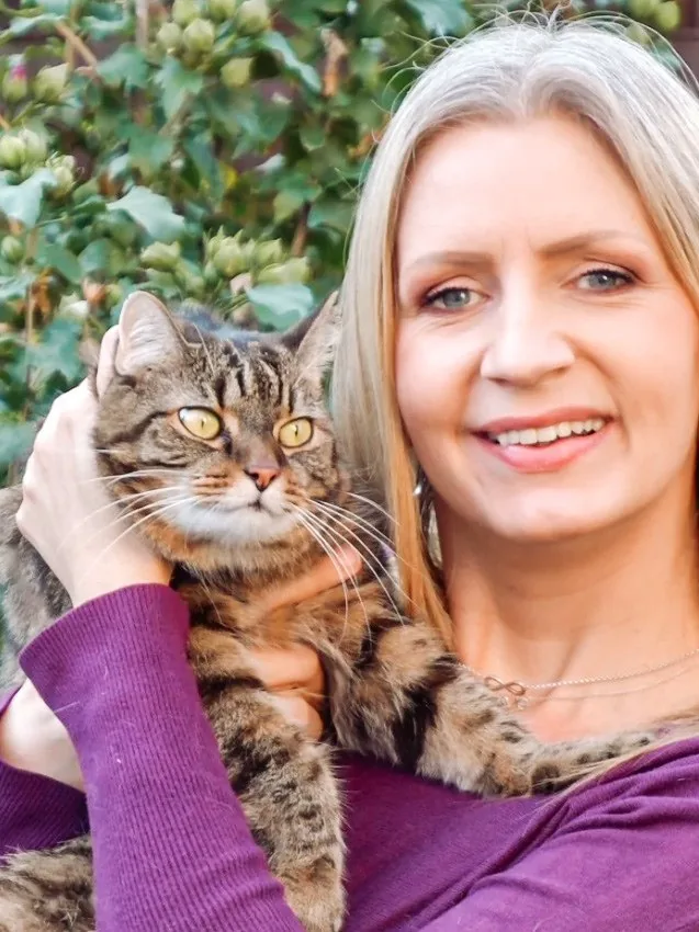 Jessica Koß lächelt in die Kamera und hält ihren getigerten Kater Tommy im Arm.